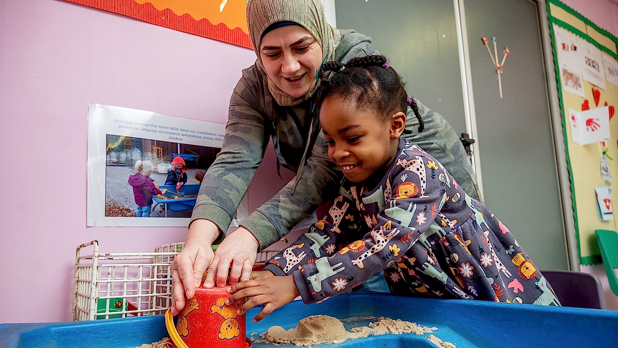 Nursery nurse helping child play in a sandpit