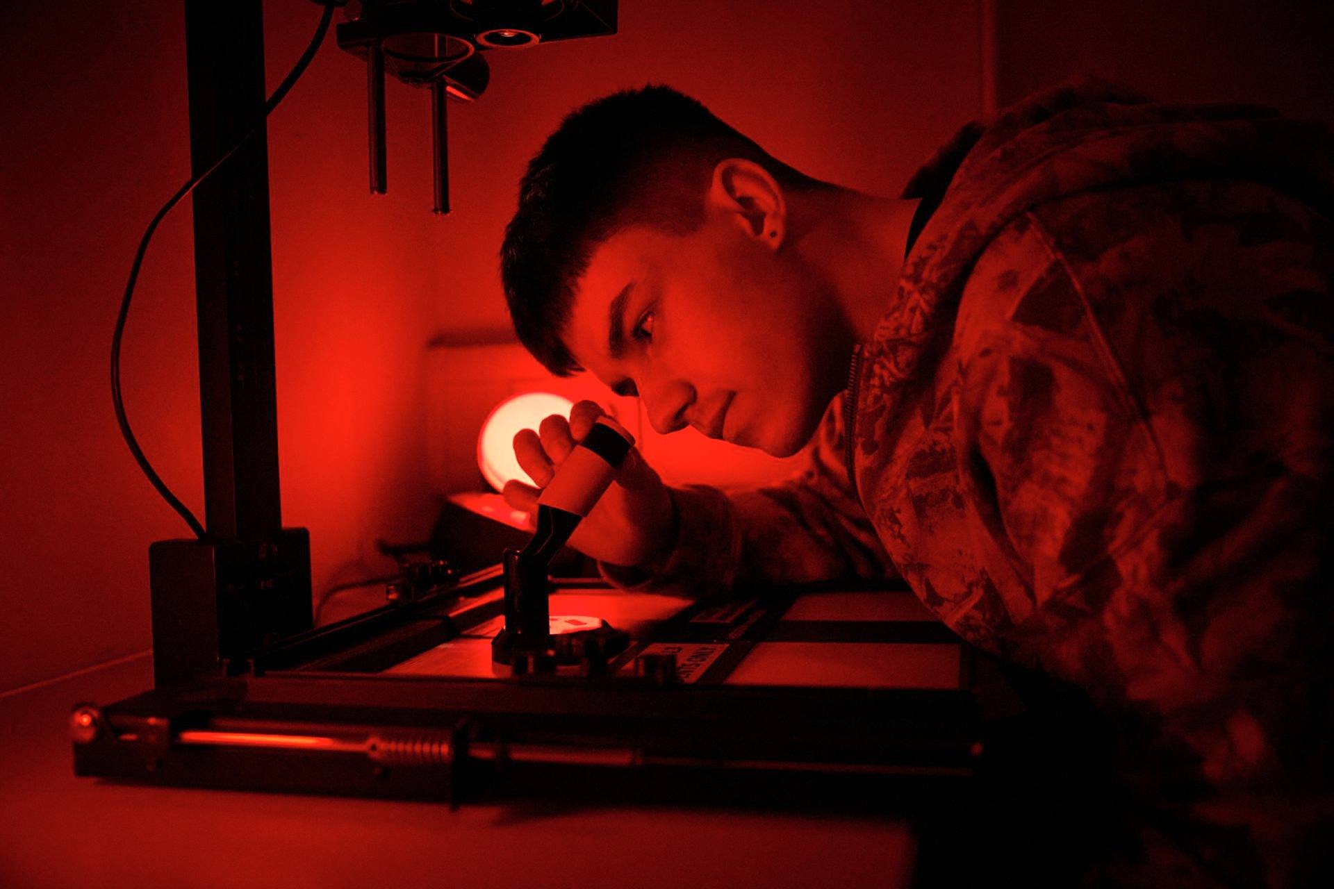 Young male adult student in photography darkroom looking at image