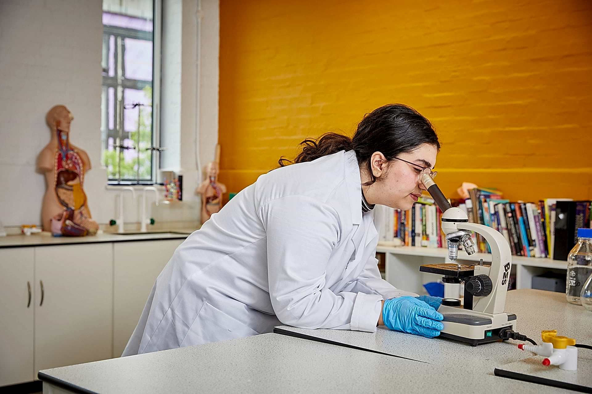 Student in science lab in white lab coat looking through microscope.