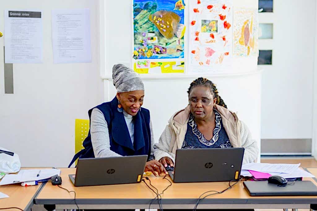 Teacher helping older female student at laptop