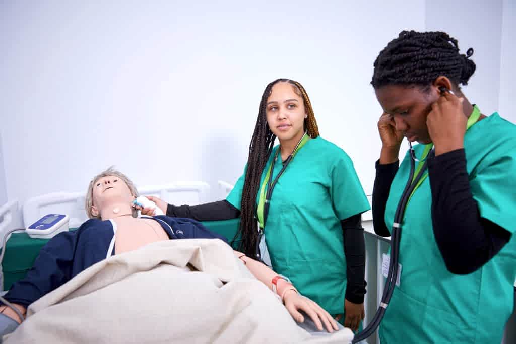 Two young female students in green wrappers in mock hospital wing